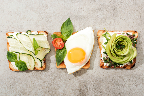 Top view of toasts with vegetables, basil and fried egg on textured surface