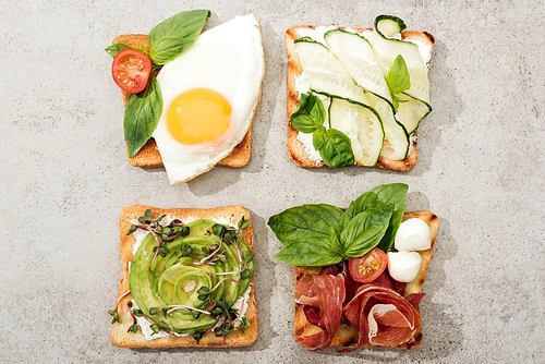 Top view of toasts with vegetables, fried egg and prosciutto on textured surface