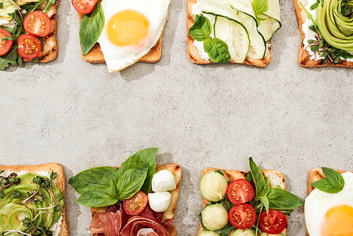 Top view of toasts with vegetables, fried eggs and prosciutto on textured surface