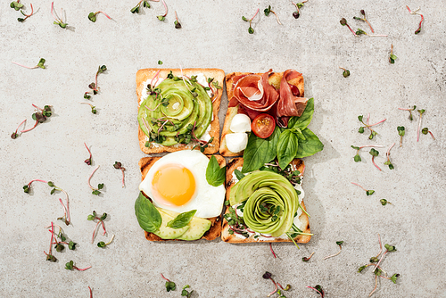 Top view of toasts with vegetables, fried egg, basil ang garden cress on textured surface