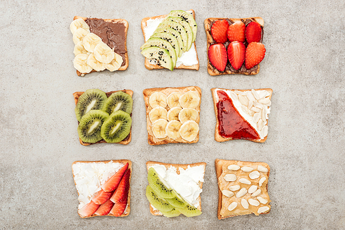 Top view of toasts with cut fruits, berries and peanuts on textured surface