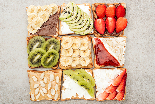 Top view of toasts with cut fruits, berries and peanuts on textured surface
