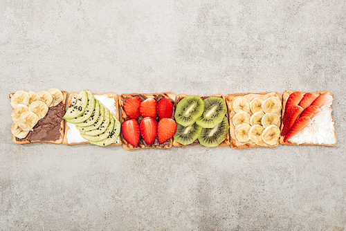 Top view of toasts with cut fruits and berries on textured surface