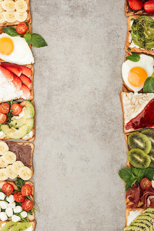 Top view of toasts with fried eggs, cut vegetables and fruits on textured surface