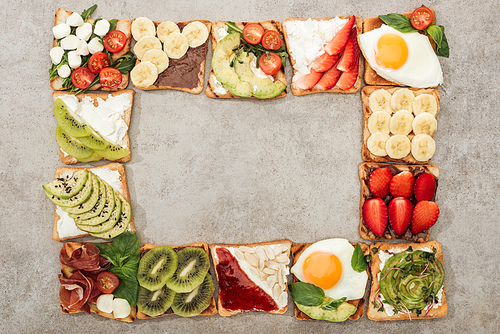 Top view of toasts with fried eggs, cut vegetables and fruits on textured surface