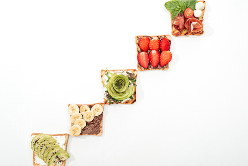 Top view of toasts with cut fruits, strawberry and prosciutto on white surface