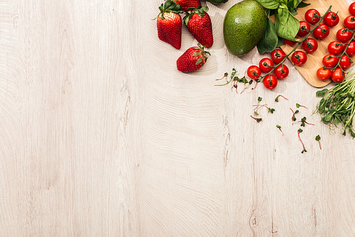 top view of strawberries, cherry tomatoes, avocado and basil on wooden table with copy space