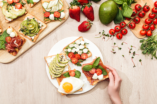 top view of woman with delicious  toasts and ingredients on wooden table