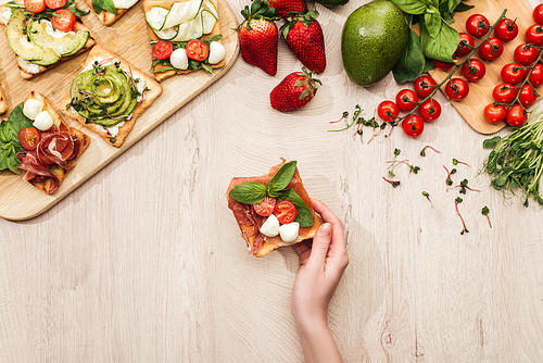 top view of woman with delicious  toasts and fresh ingredients on wooden table