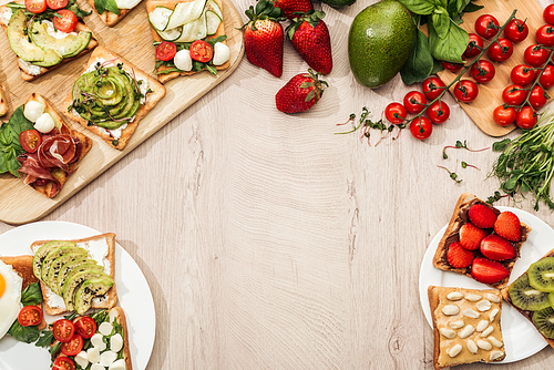 top view of toasts with s, fruits and prosciutto with greenery and ingredients on wooden table