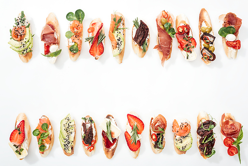 top view of traditional italian bruschetta with prosciutto, salmon, fruits, s and herbs on white with copy space