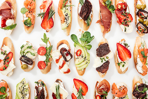 background of delicious italian bruschetta with salmon, prosciutto, dried tomatoes, avocado, strawberries and herbs on white