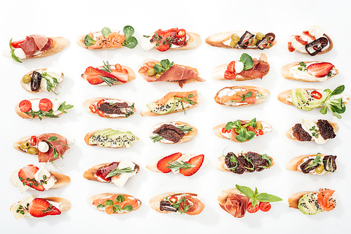 background of italian bruschetta with salmon, prosciutto, dried tomatoes, avocado, strawberries and herbs on white