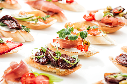selective focus of italian bruschetta with dried tomatoes, prosciutto and herbs on white