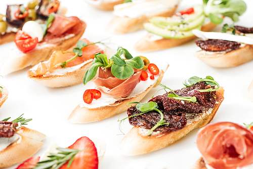 selective focus of italian bruschetta with dried tomatoes, prosciutto, salmon and herbs on white