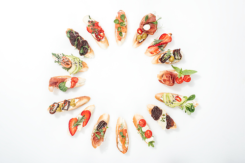 top view of round frame made of traditional italian bruschetta with salmon, prosciutto, herbs and various fruits with s