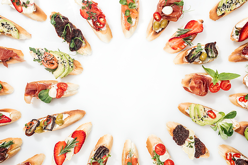 top view of round frame made of italian bruschetta with salmon, prosciutto, herbs and various fruits with s on white