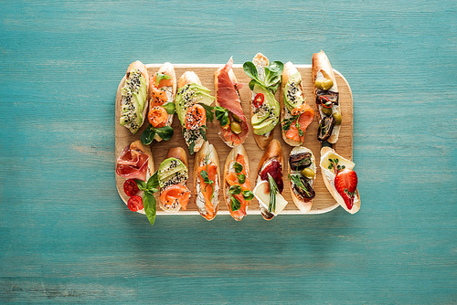 top view of italian bruschetta with prosciutto, salmon and vegetables on chopping board