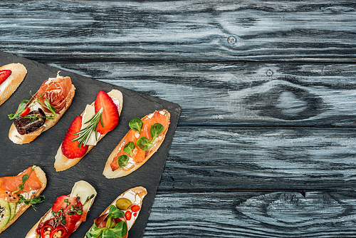 top view of italian bruschetta with strawberries, salmon and prosciutto on chopping board with copy space