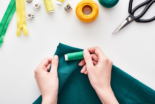 top view of seamstress holding colorful fabric and threads on white background