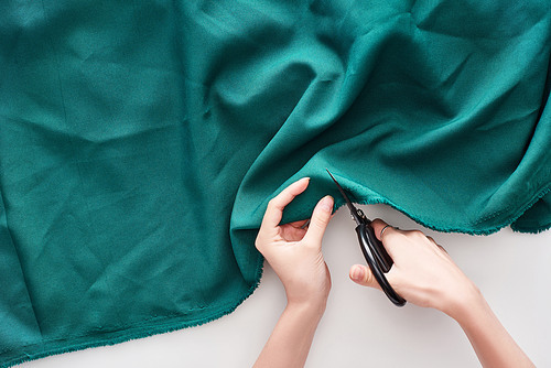 top view of seamstress cutting colorful fabric with scissors on white background