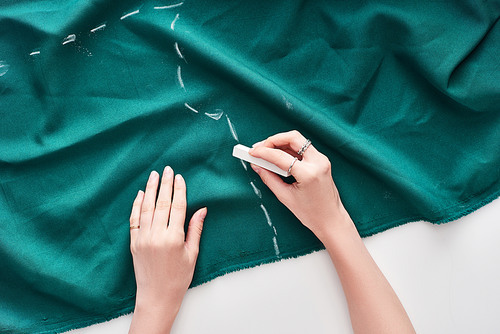 top view of seamstress drawing on colorful fabric with chalk on white background