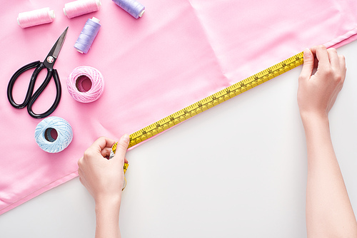 cropped view of seamstress measuring fabric with measuring tape on white background