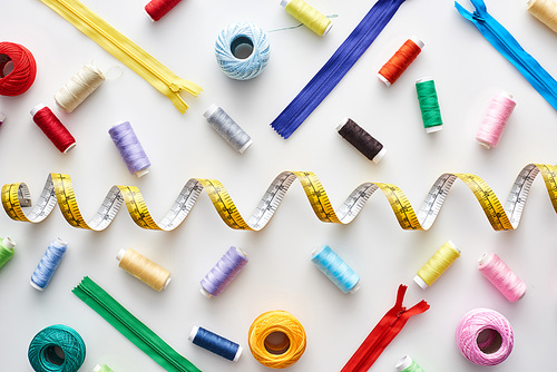 top view of measuring tape, colorful threads and zippers on white background