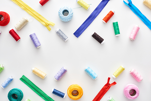 top view of colorful threads, knitting yarn balls and zippers on white background