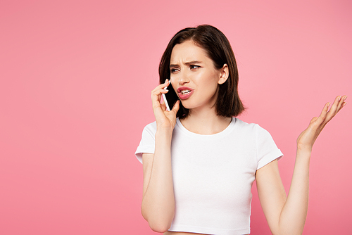 displeased girl talking on smartphone isolated on pink