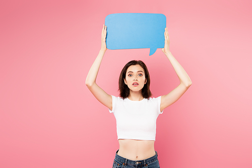 surprised pretty girl holding blank blue speech bubble isolated on pink