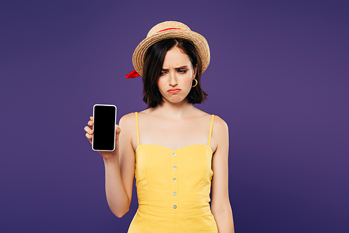 sad pretty girl in straw hat holding smartphone with blank screen isolated on purple