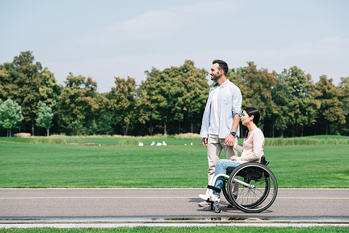 handsome young man holding hands with disabled girlfriend while walking in park together