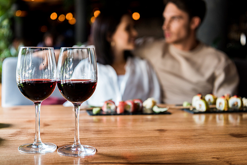 selective focus of glasses with red wine near happy man and woman