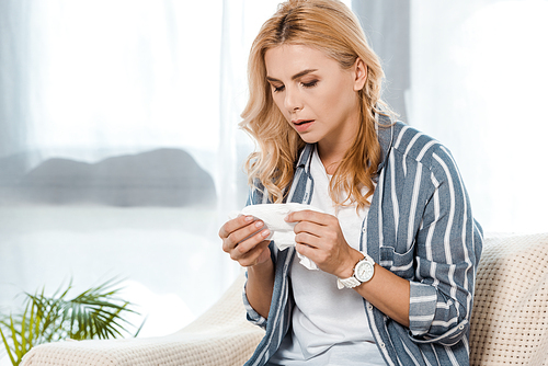 sick woman sitting on sofa and looking at napkin