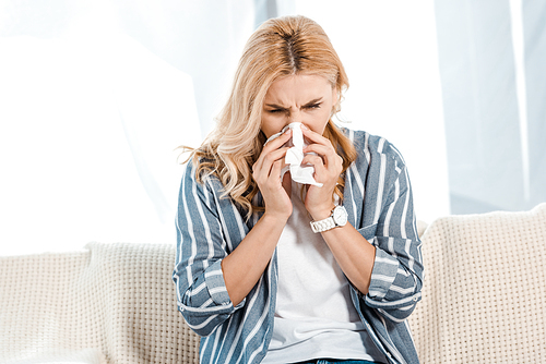 sick woman sitting on sofa and sneezing in napkin