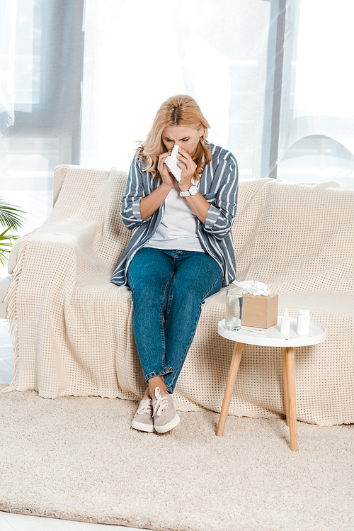 sick woman sitting on sofa and sneezing in napkin near tissue box