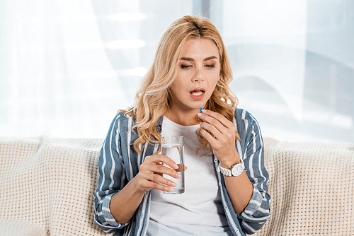 woman taking pill while holding glass with water