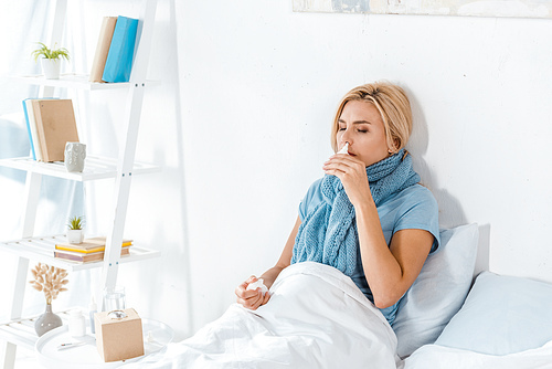 sick woman holding nasal spray near nose while lying in bed