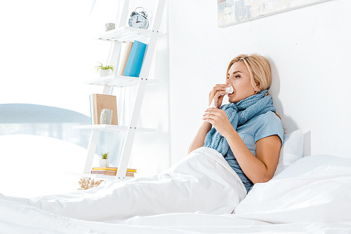 sick woman holding tissue near nose while lying in bed