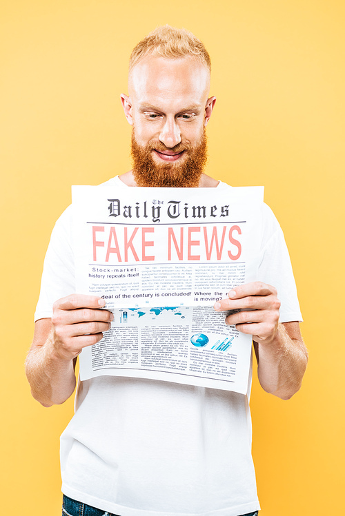 smiling bearded man reading newspaper with fake news, isolated on yellow