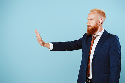 serious bearded businessman in suit showing stop sign, isolated on blue