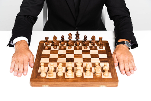 cropped view of businessman in suit sitting near chessboard isolated on grey