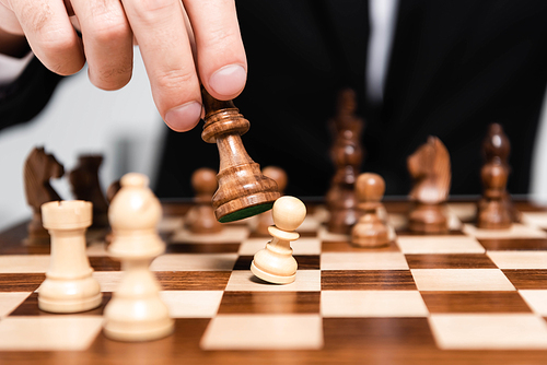 cropped view of businessman holding chess figure above chessboard