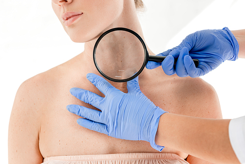 cropped view of dermatologist examining skin of patient with magnifying glass in clinic