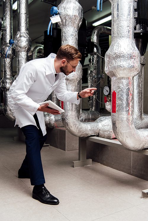 engineer in white coat holding digital tablet and pointing with finger at air supply system