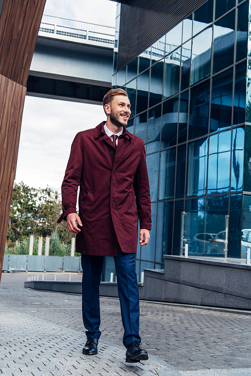 cheerful bearded man in coat walking on street