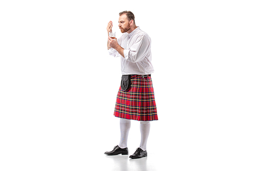 Scottish redhead man in red kilt smelling whiskey on white