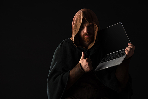 medieval Scottish redhead man in mantel holding laptop and showing thumb up in dark isolated on black