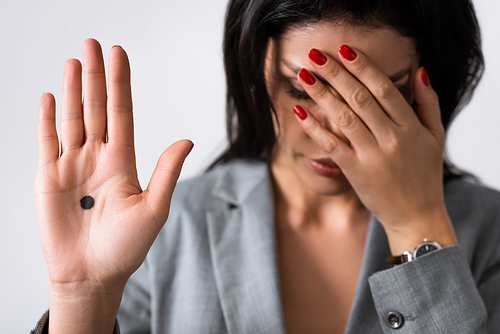 selective focus of sad businesswoman showing hand with black dot on palm and covering eyes isolated on white, domestic violence concept